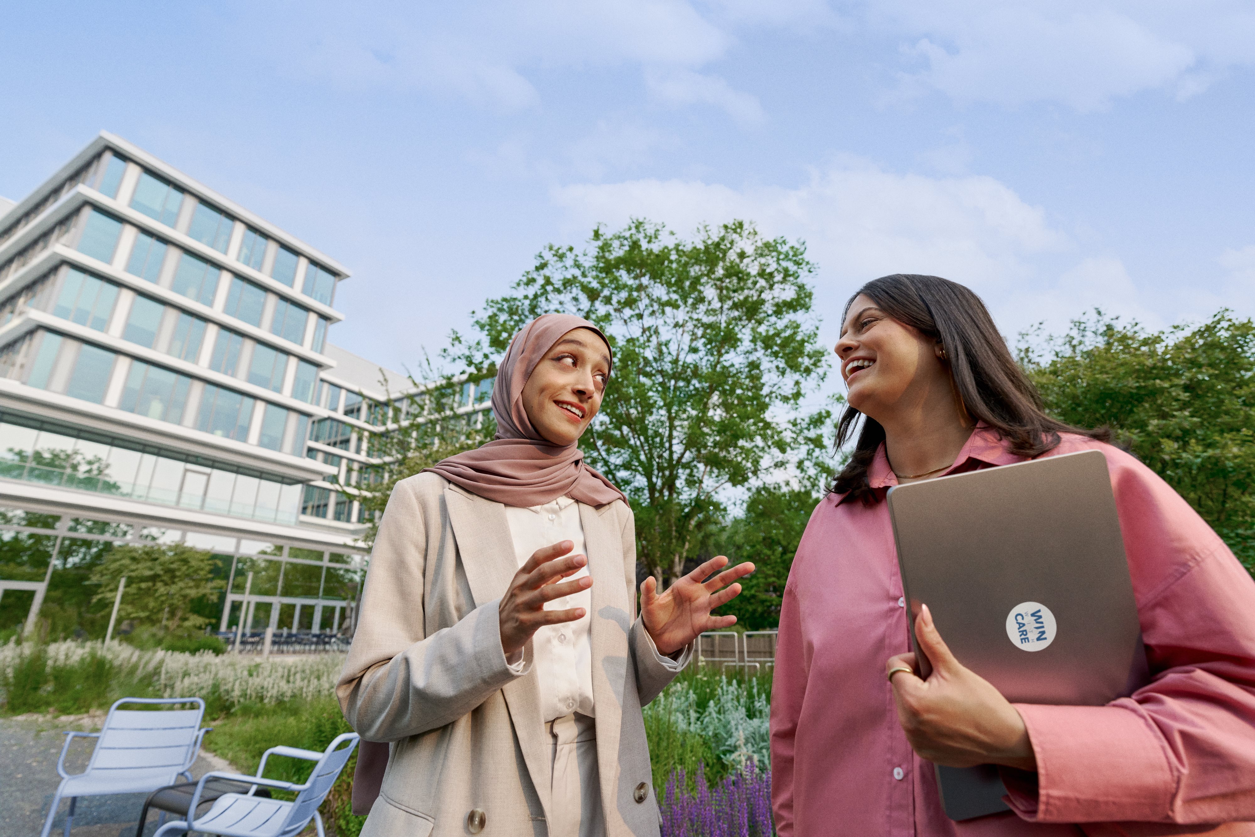 Two colleagues smiling and talking outdoors on campus.