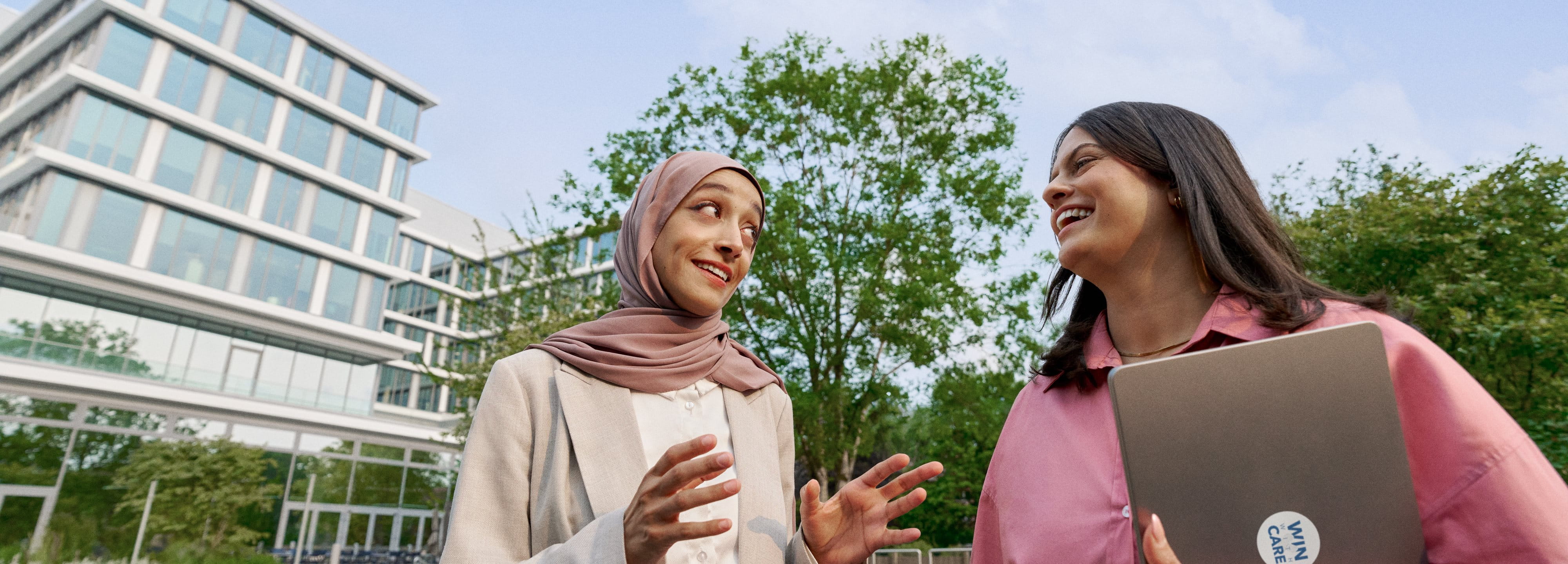 Two colleagues smiling and talking outdoors on campus.