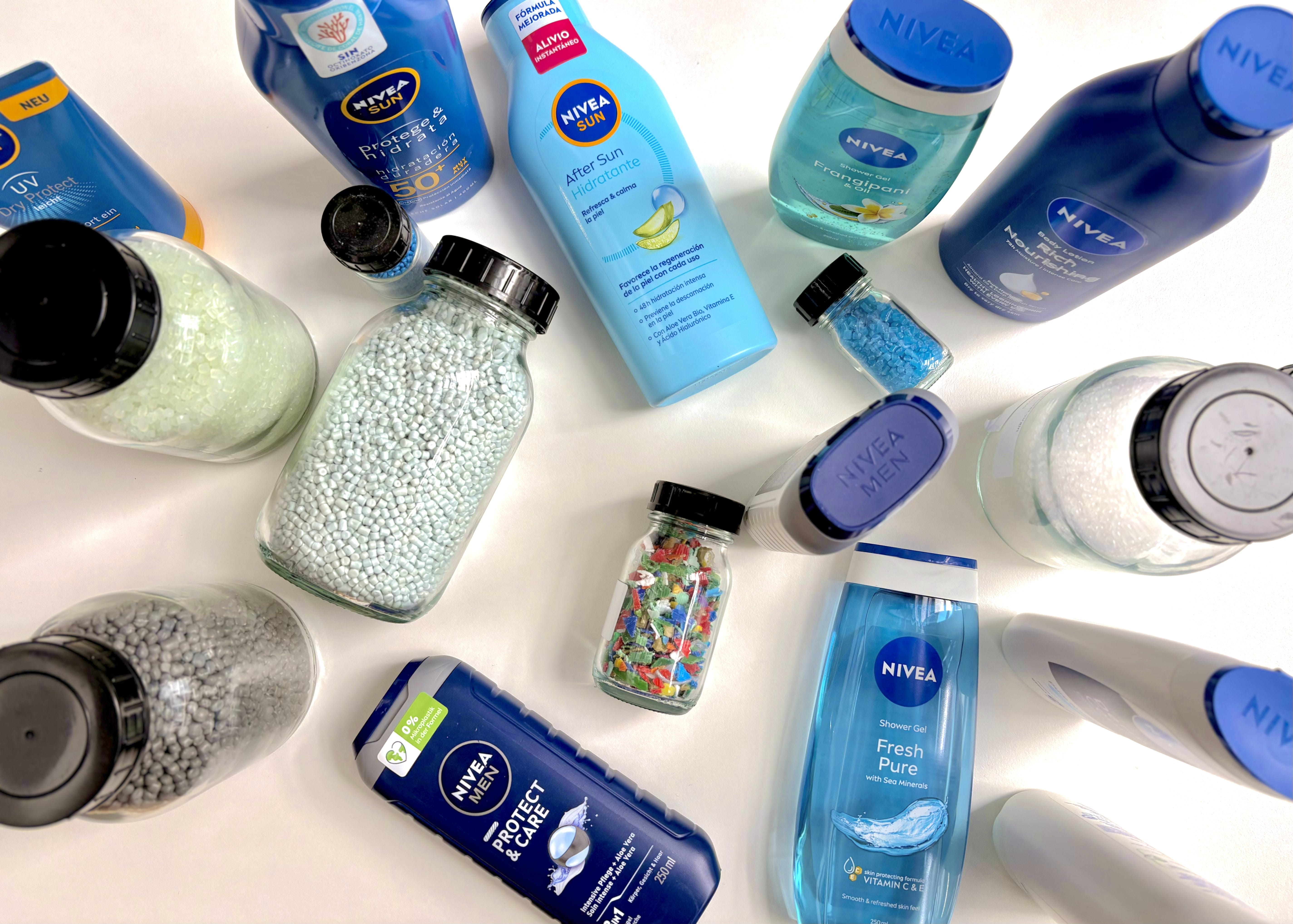 NIVEA personal care and sun care products arranged in a circular layout around jars containing recycled plastic pellets and plastic flakes, illustrating sustainable packaging innovation and the use of recycled materials in plastic packaging.