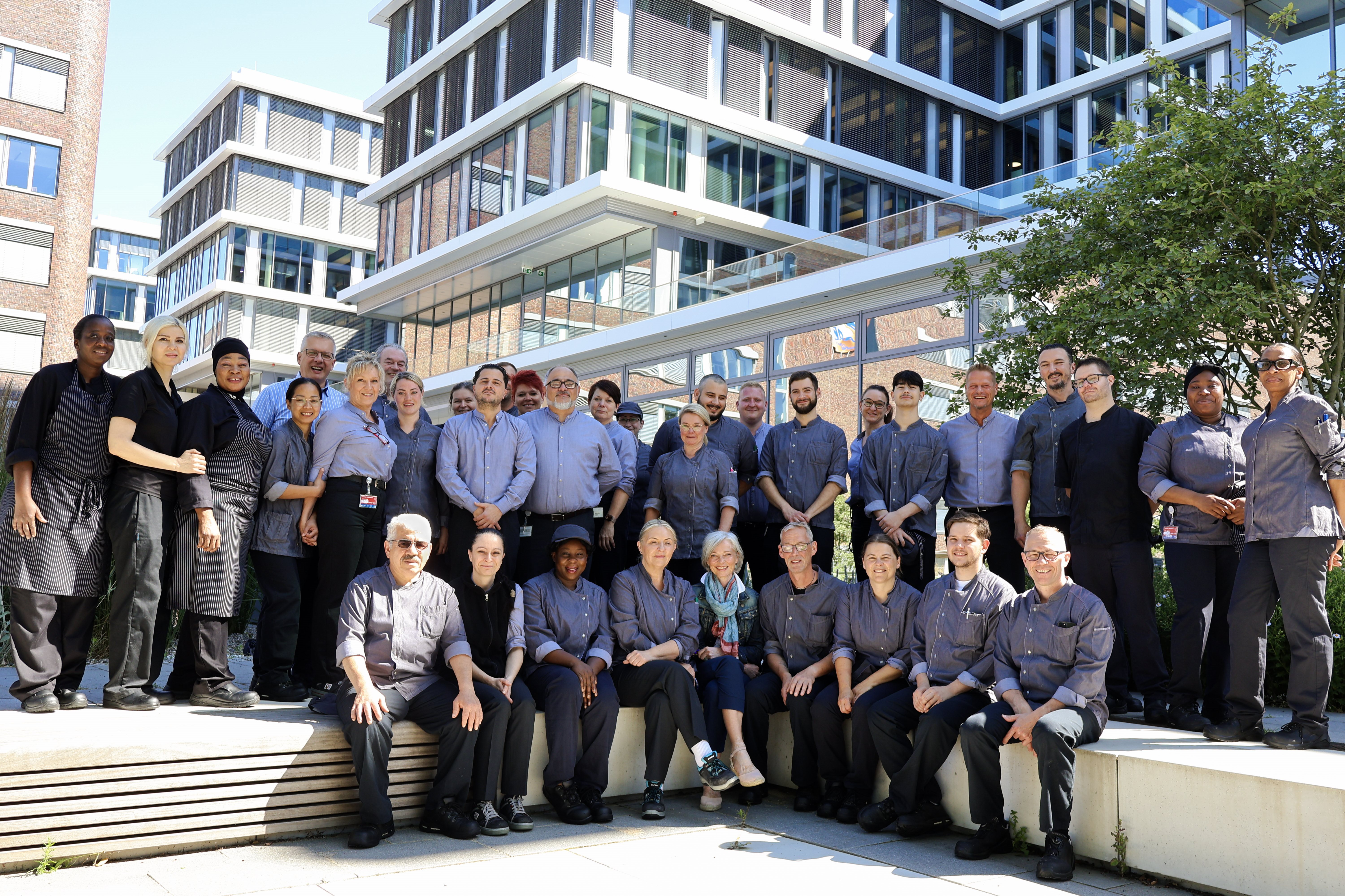 Large group of people gathered outdoors in front of a modern building, posing together for a group photo.
