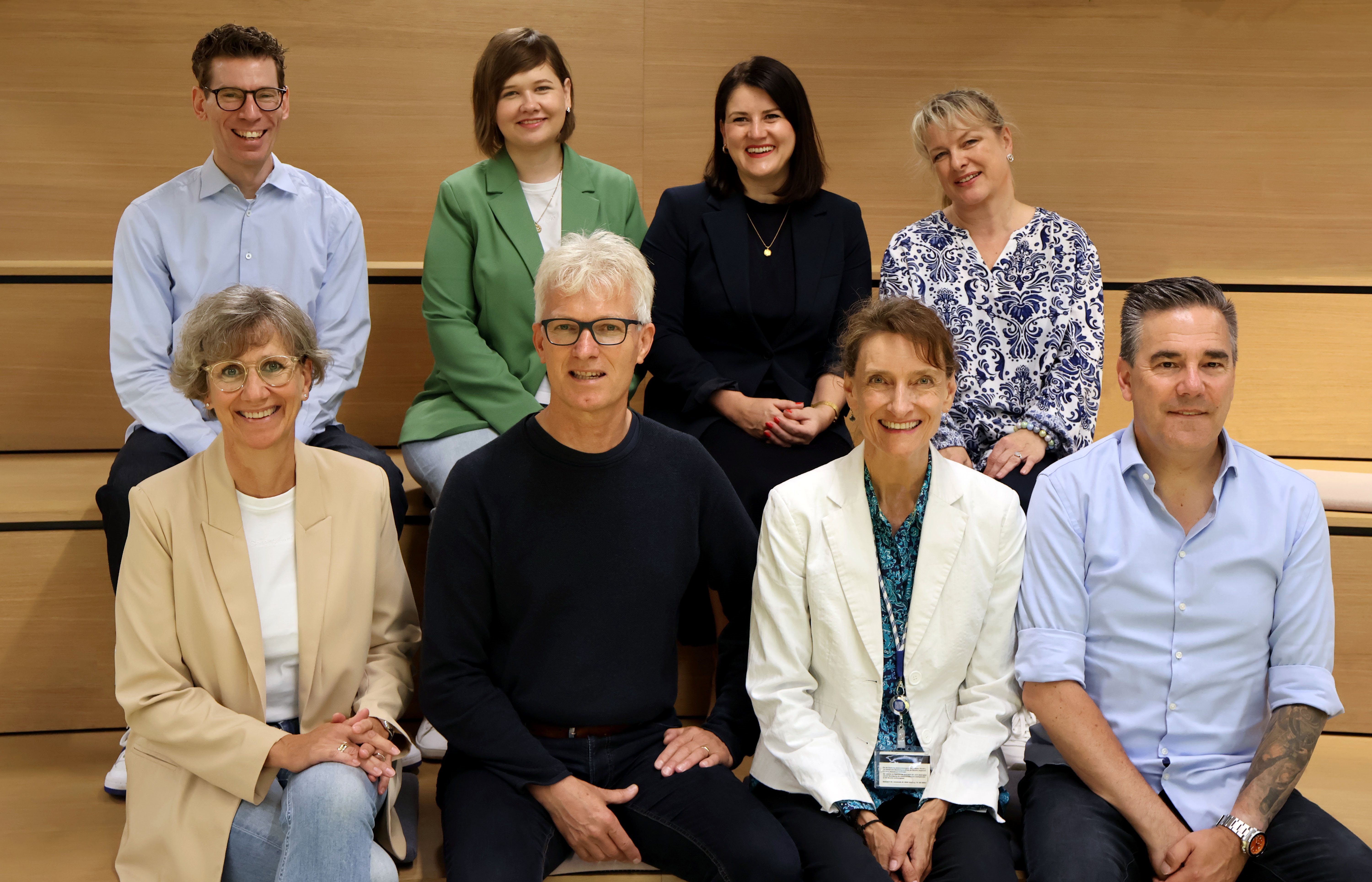 Group of people seated and standing indoors in a lecture or meeting space, posing together and smiling.