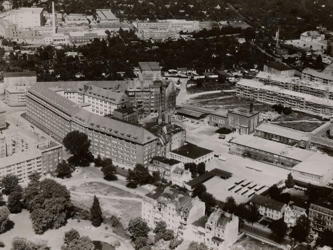 Historic black-and-white aerial photograph of a large institutional campus with long rectangular buildings, open courtyards and surrounding trees.