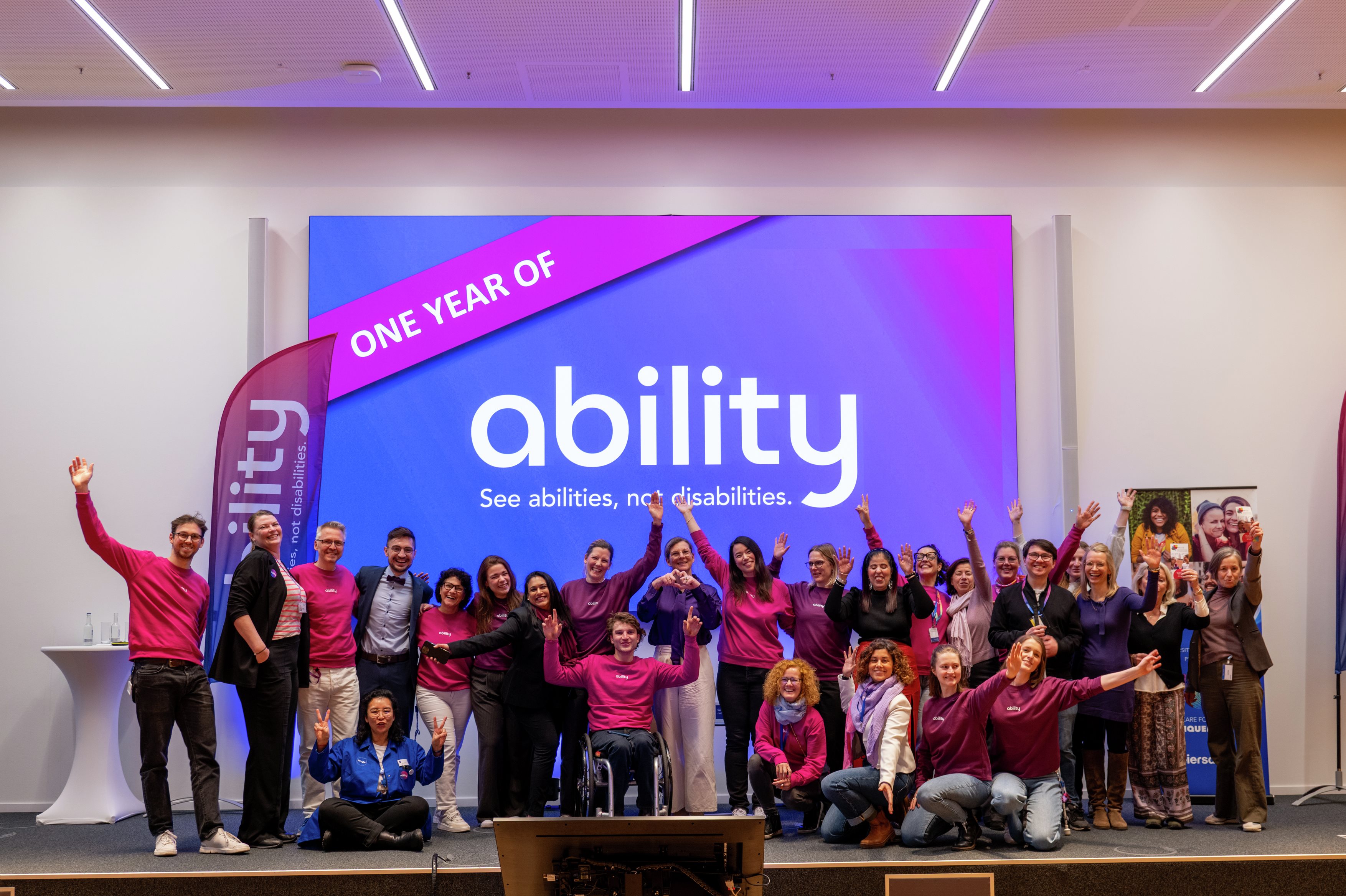 A big group of colleagues on a stage cheering, wearing purple, and celebrating the Ability employee community anniversary
