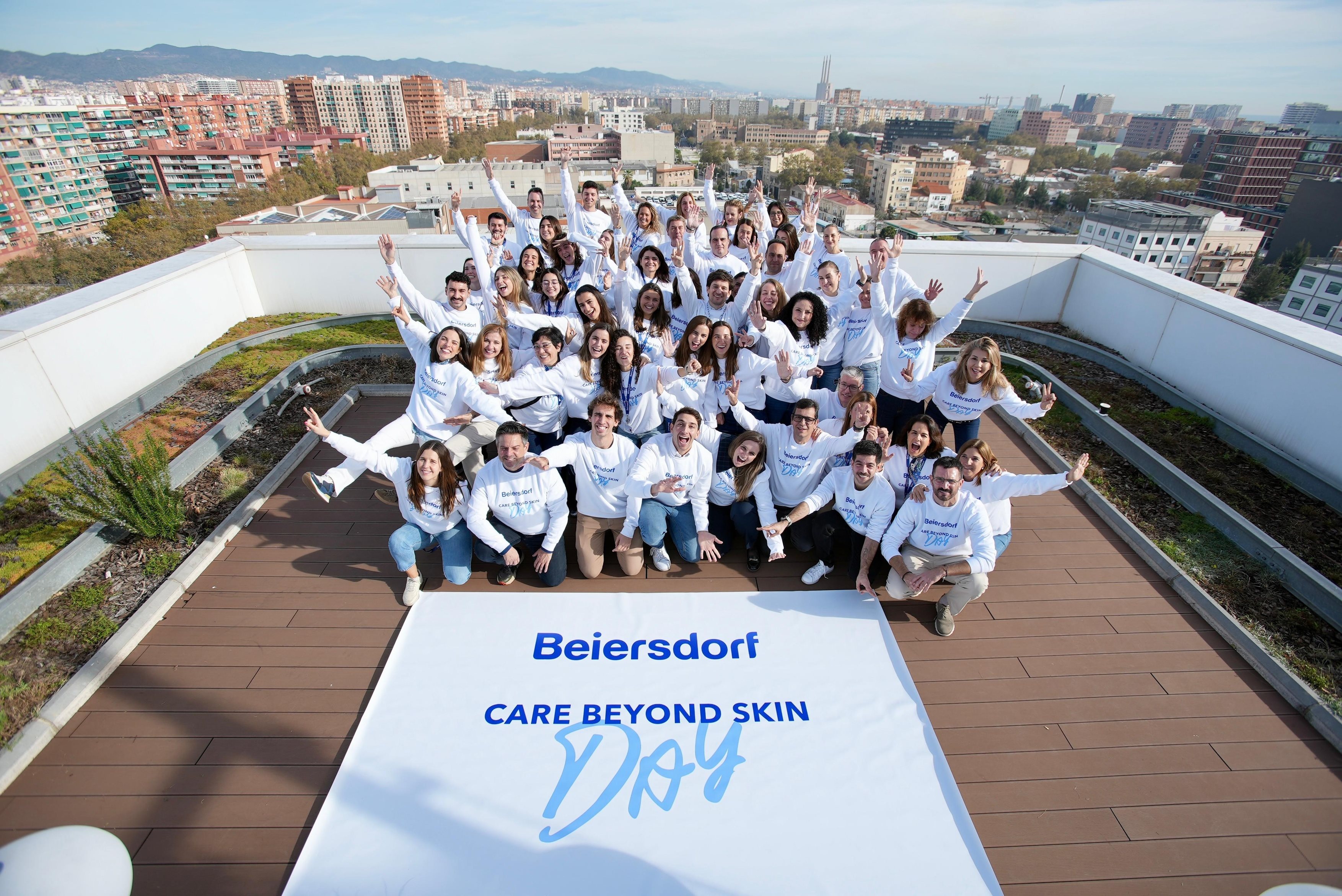 A group of colleagues posing standing and sitting on a rooftop terrace with a Beiersdorf CARE BEYOND SKIN Day banner lying in front of them