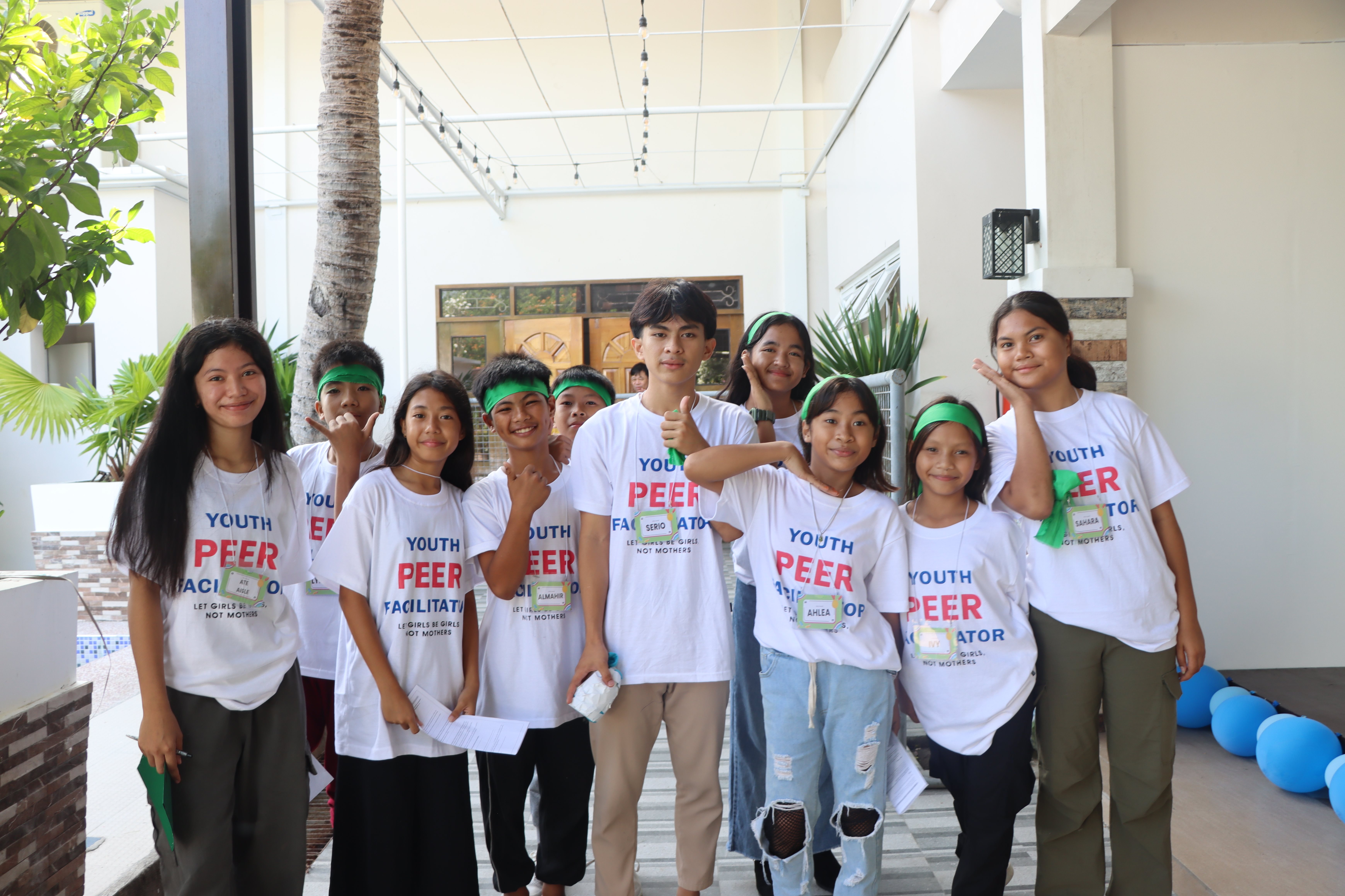 A group of teenagers in white shirts with “Youth Peer Facilitator” written on it, standing next to each other smiling