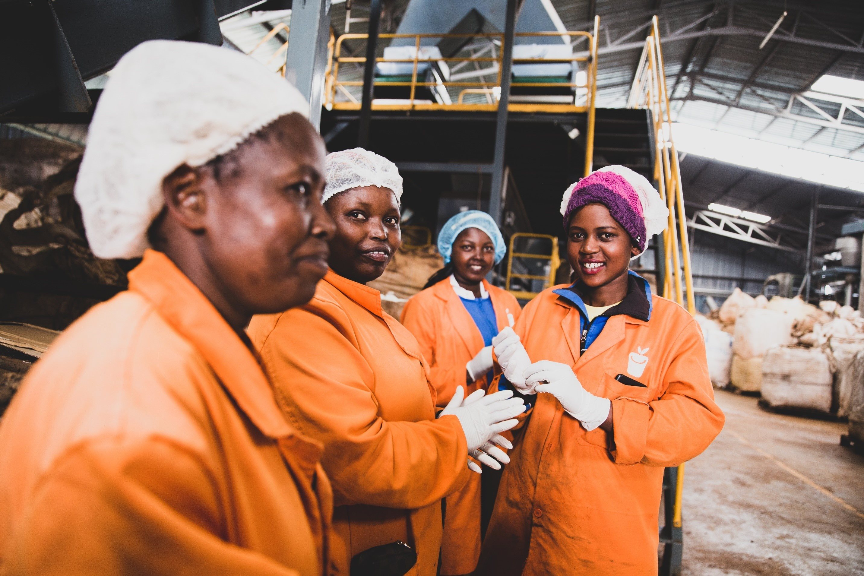 Four female waste workers in orange uniform and with safety hats standing next to each other smiling