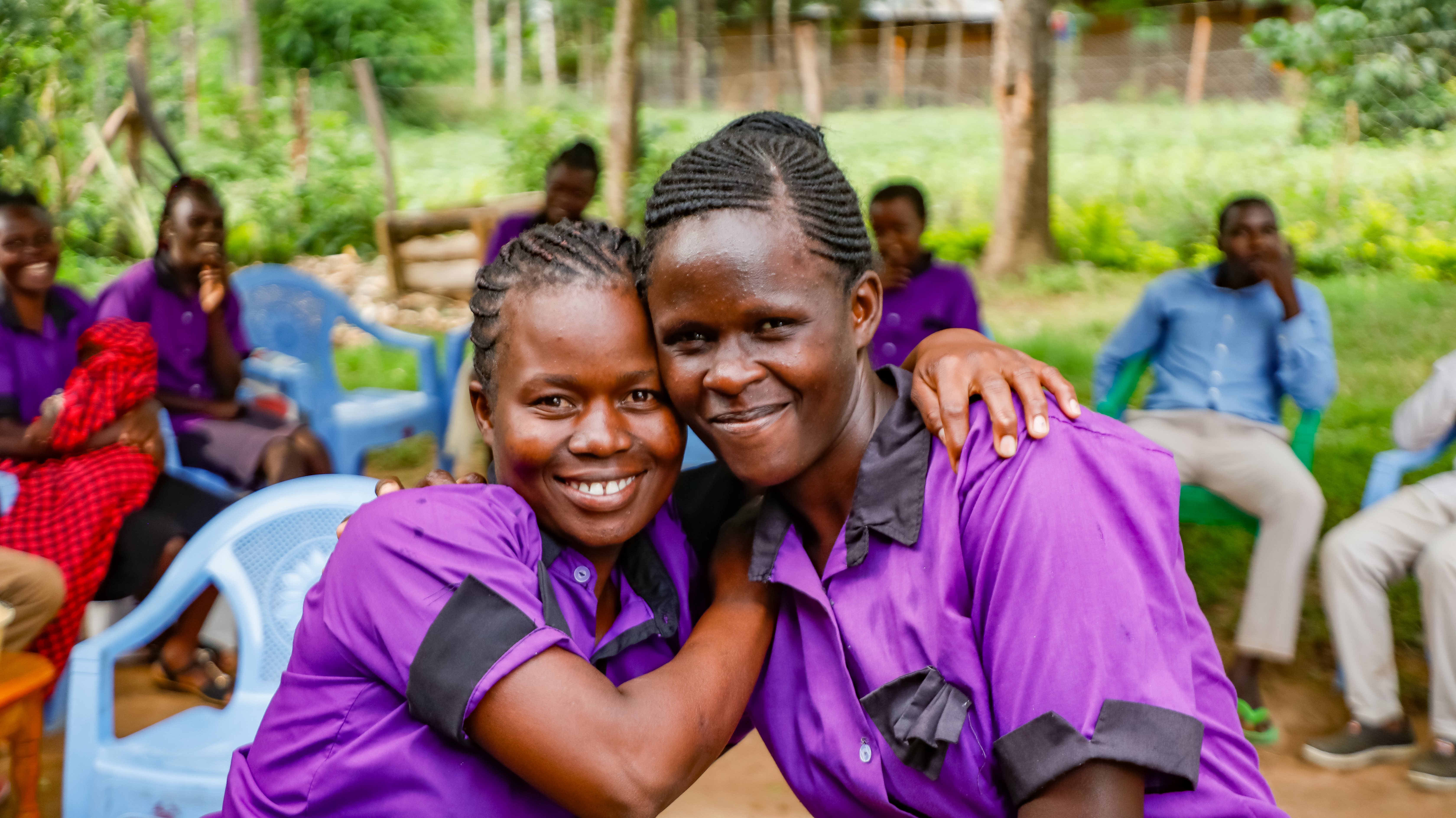 Two women in purple clothing hugging and smiling into the camera