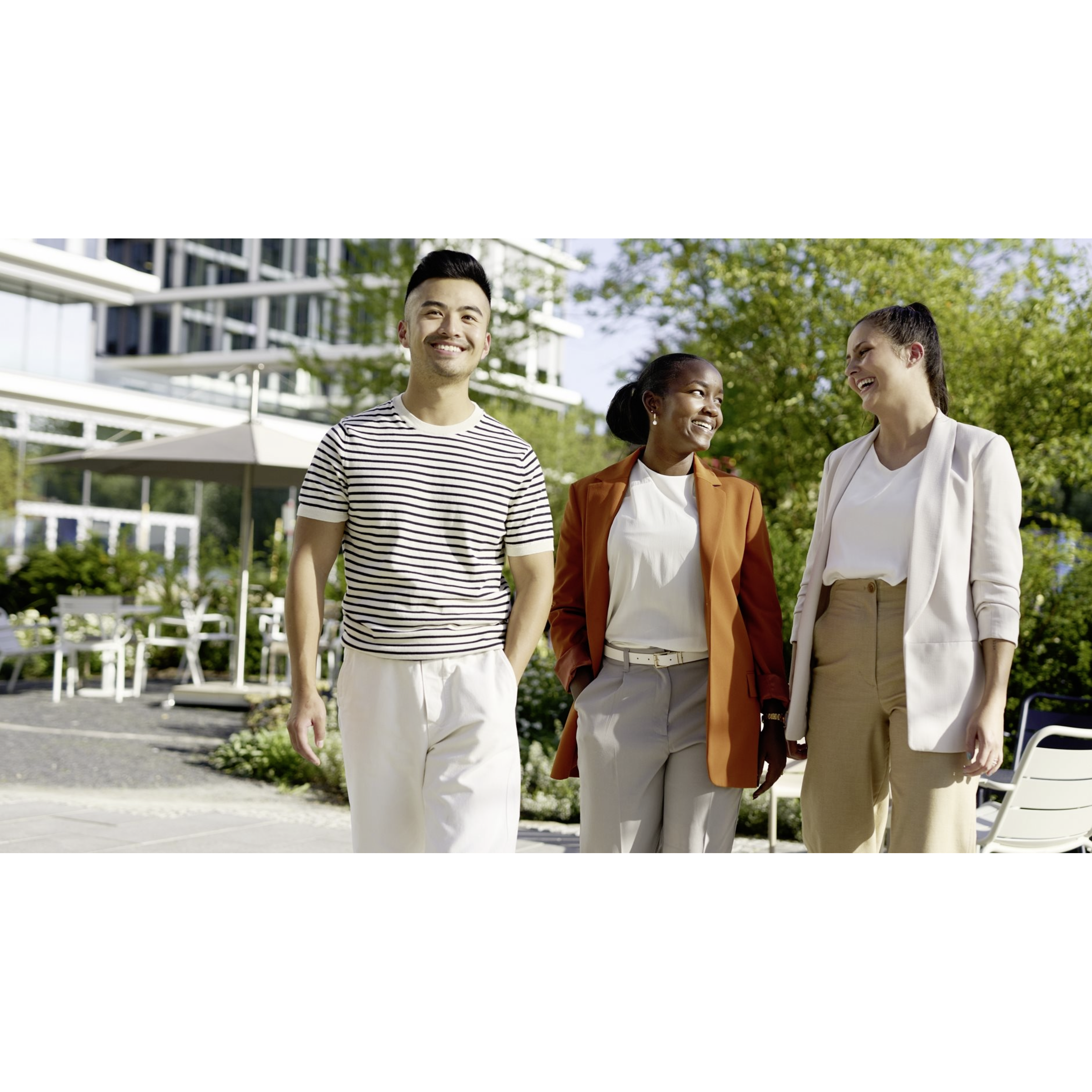 Three colleagues walking together outside an office building on a sunny day.