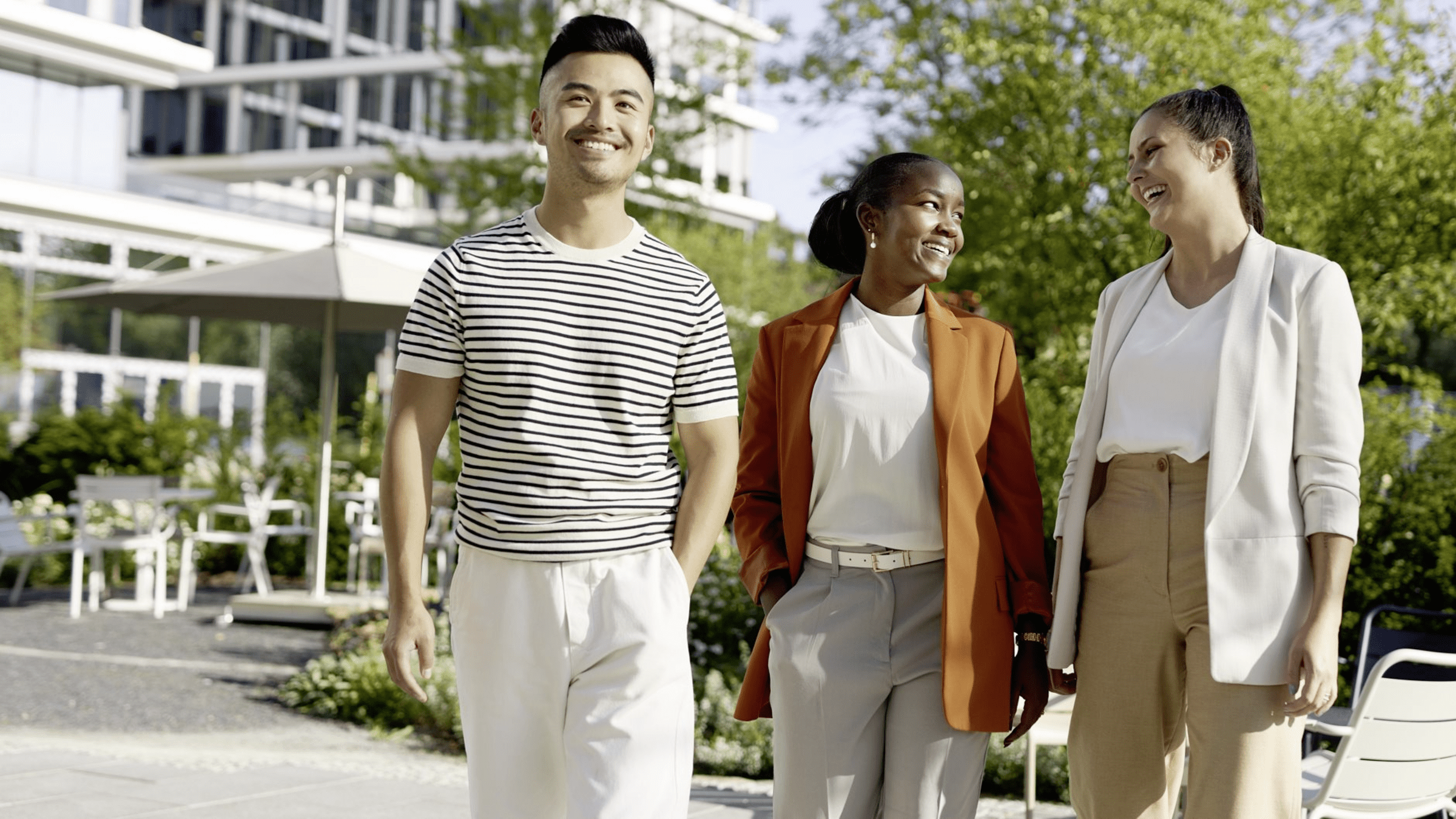 Three colleagues walking together outside an office building on a sunny day.