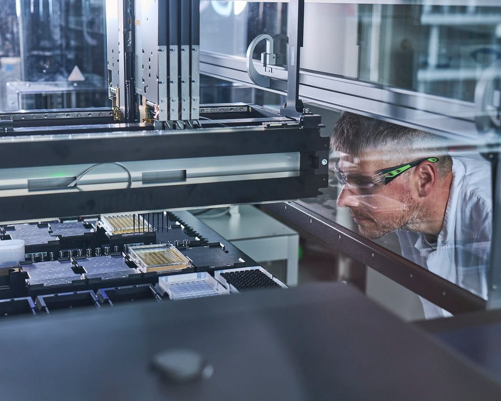 Scientist wearing safety glasses closely inspecting laboratory equipment inside a research facility, focusing on a precision experiment.
