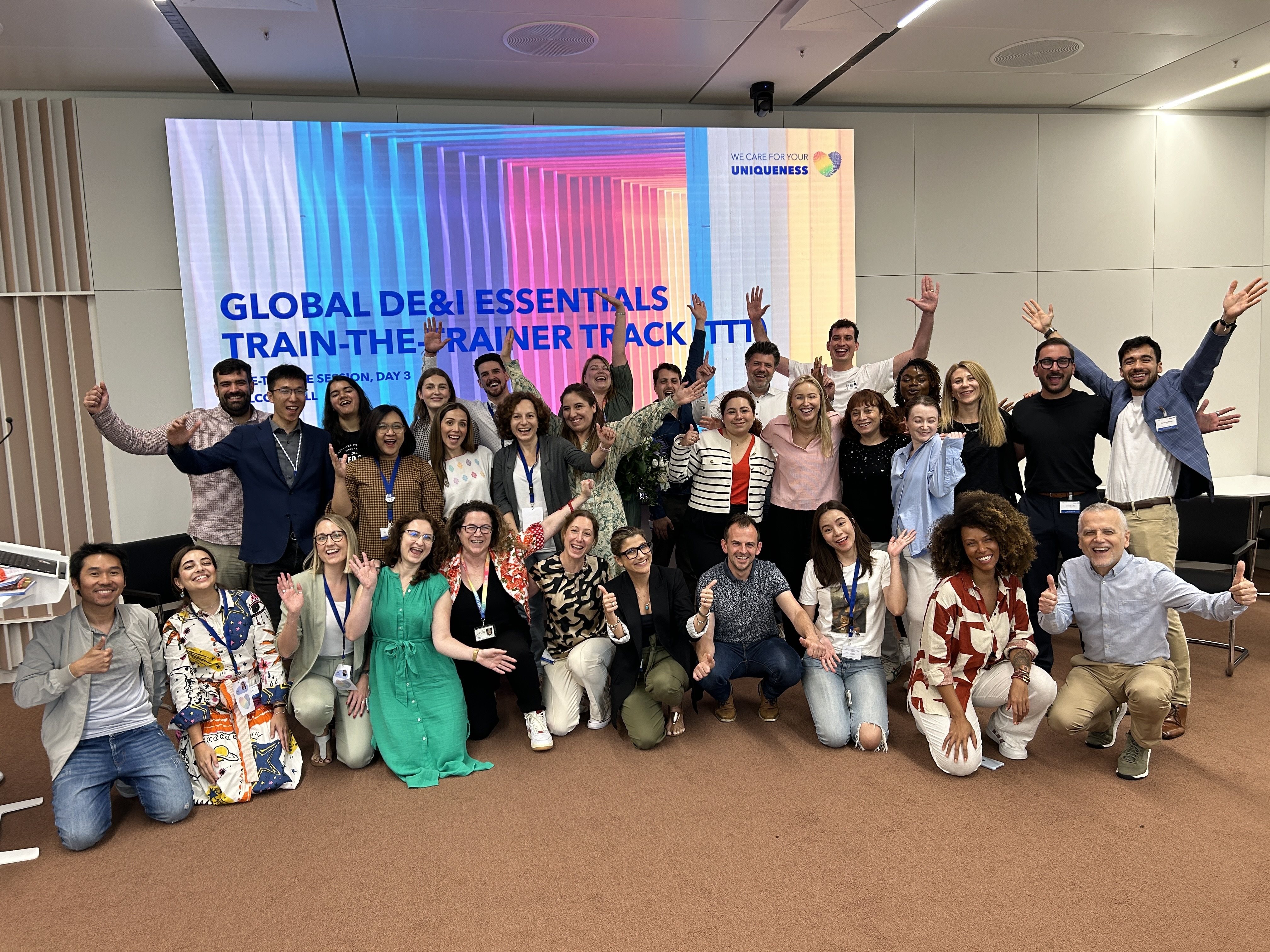A big group of colleagues cheering in front of a screen at an inclusive leadership training session.