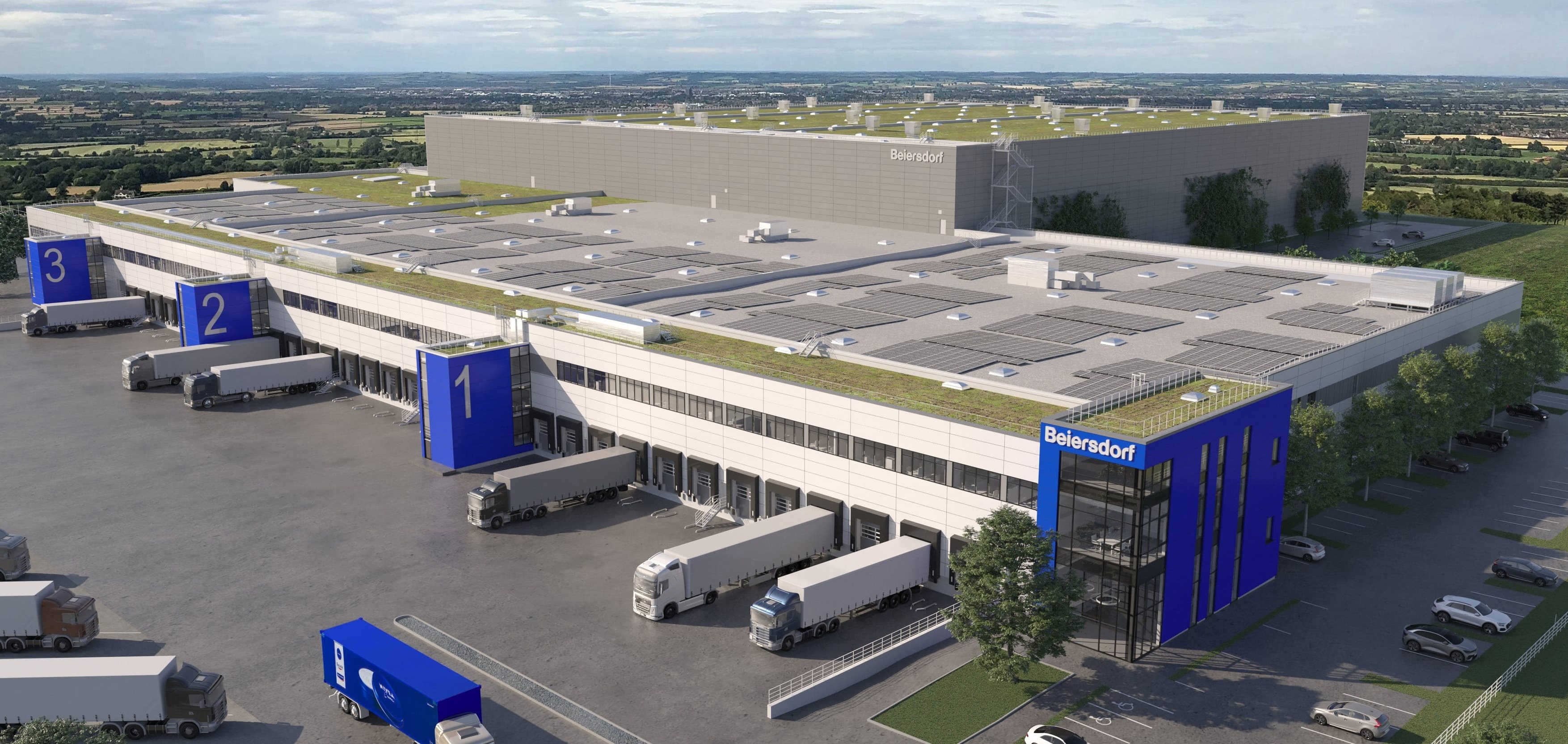 Aerial view of a large Beiersdorf logistics and distribution center with multiple loading bays, parked trucks, blue-branded buildings, and green roofs fitted with solar panels, set within a rural landscape.