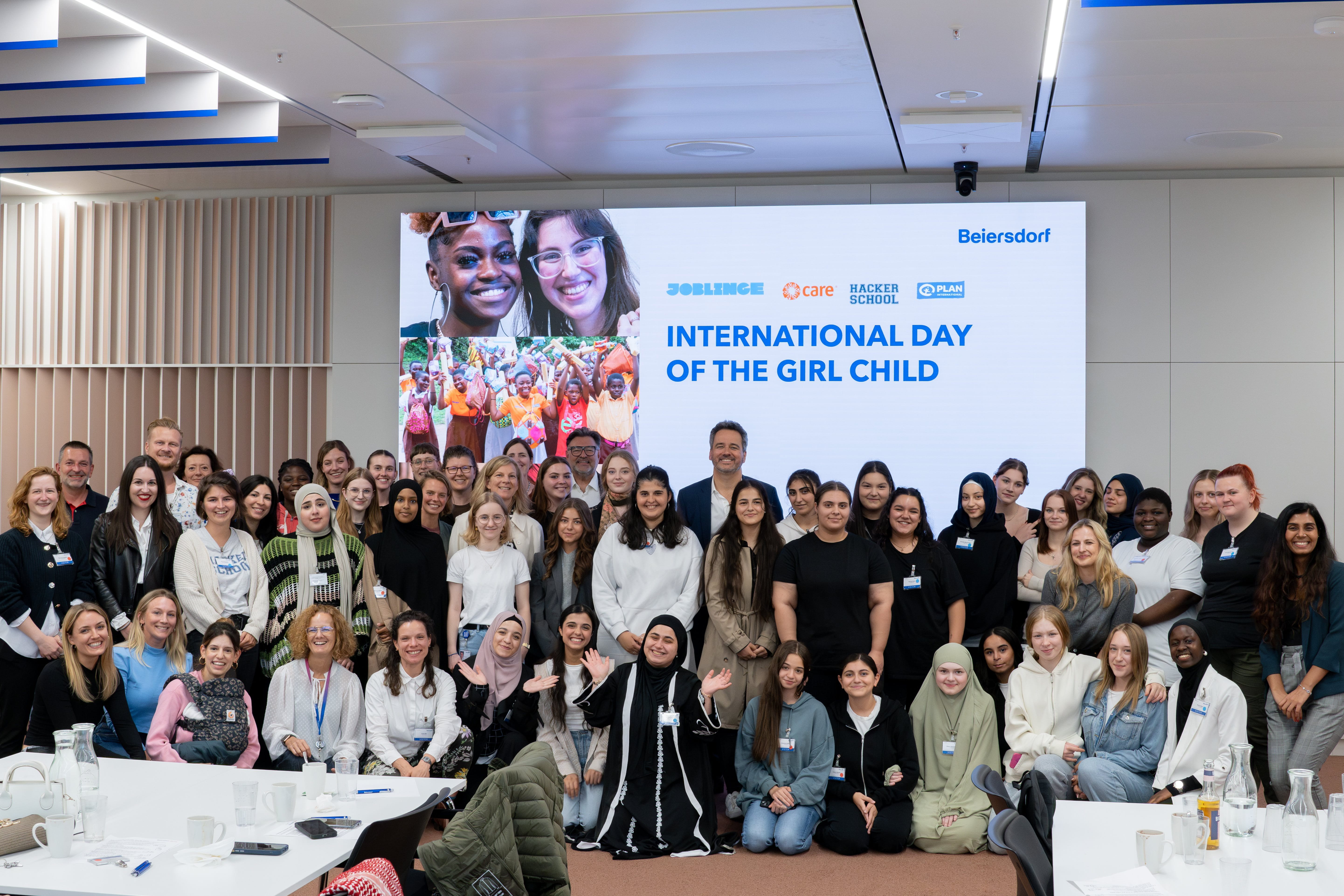Large group of participants posing together at a Beiersdorf event, standing in front of a screen reading ‘International Day of the Girl Child,’ celebrating girls’ empowerment and inclusion.