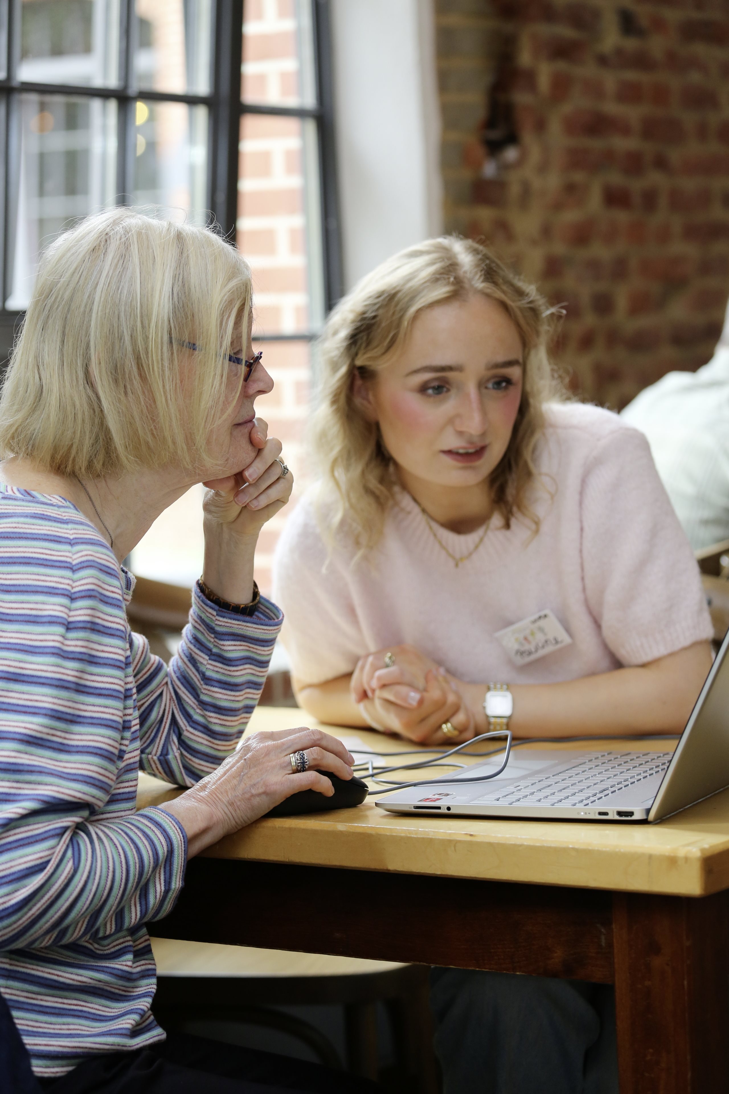 A young and an elderly woman looking at a computer screen in an urban community space during Beiersdorf’s CARE BEYOND SKIN Day.