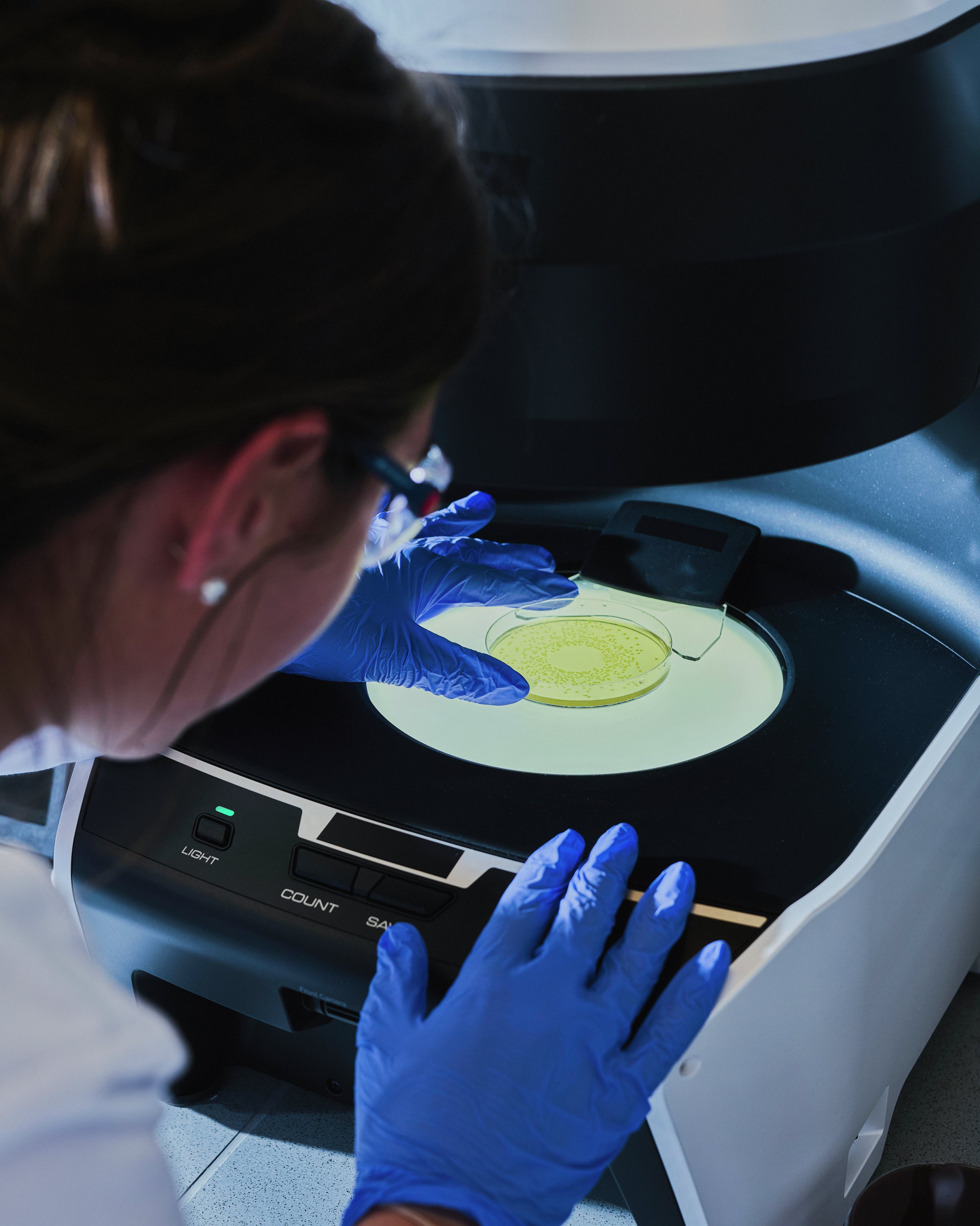 Scientist wearing blue gloves placing a sample dish into a laboratory analysis device, carefully positioning it for testing.